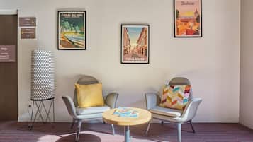 Un hall d’hôtel avec deux fauteuils, une table ronde et trois affiches encadrées accrochées au mur.