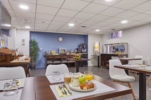 Ein Hotel-Essbereich mit gedeckten Tischen für das Frühstück, einer Uhr an der Wand und einer Küchenzeile im Hintergrund.