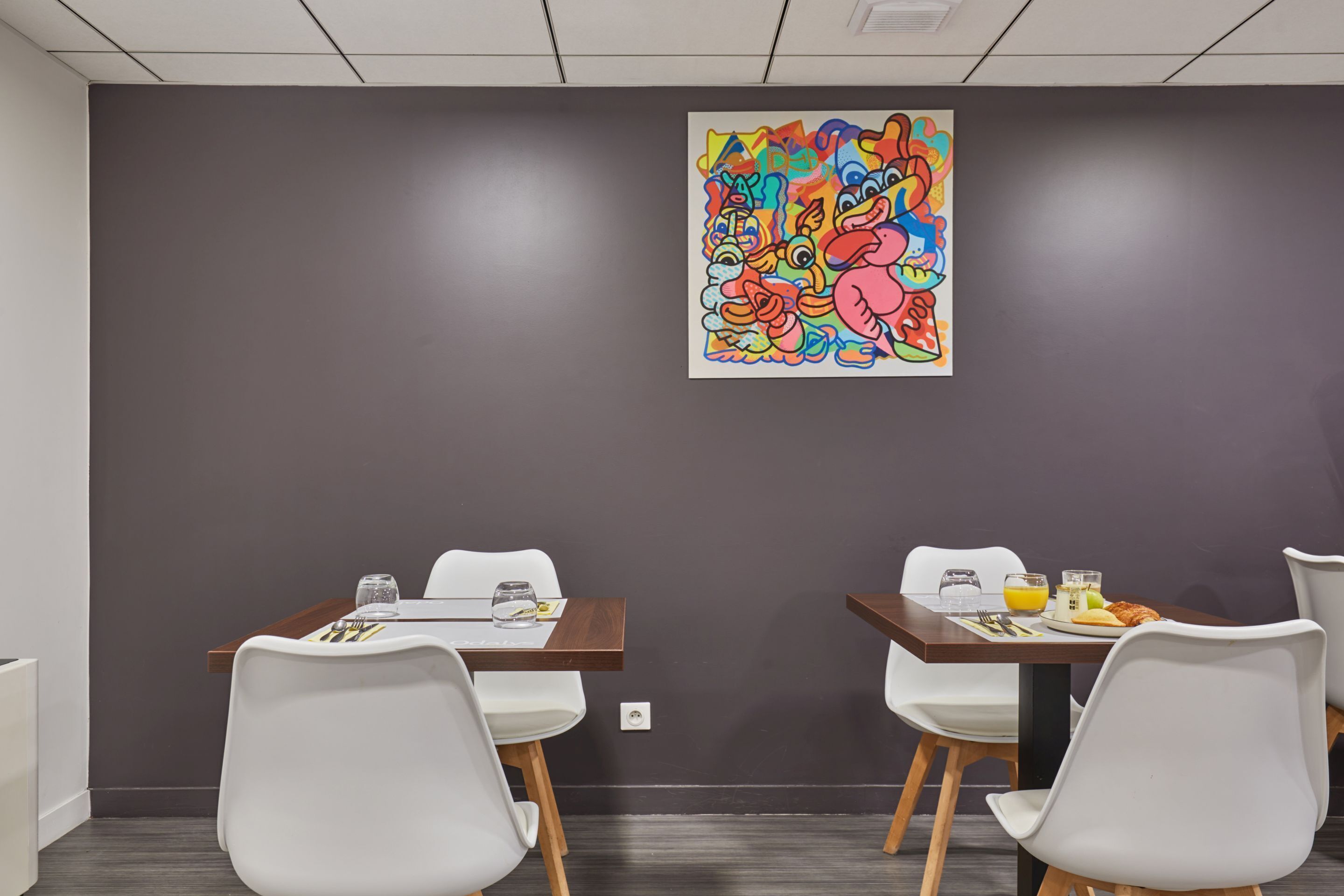 Una sala de conferències amb dues taules, cadires blanques i un quadre abstracte i colorit a la paret.