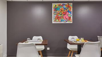 Una sala de conferències amb dues taules, cadires blanques i un quadre abstracte i colorit a la paret.