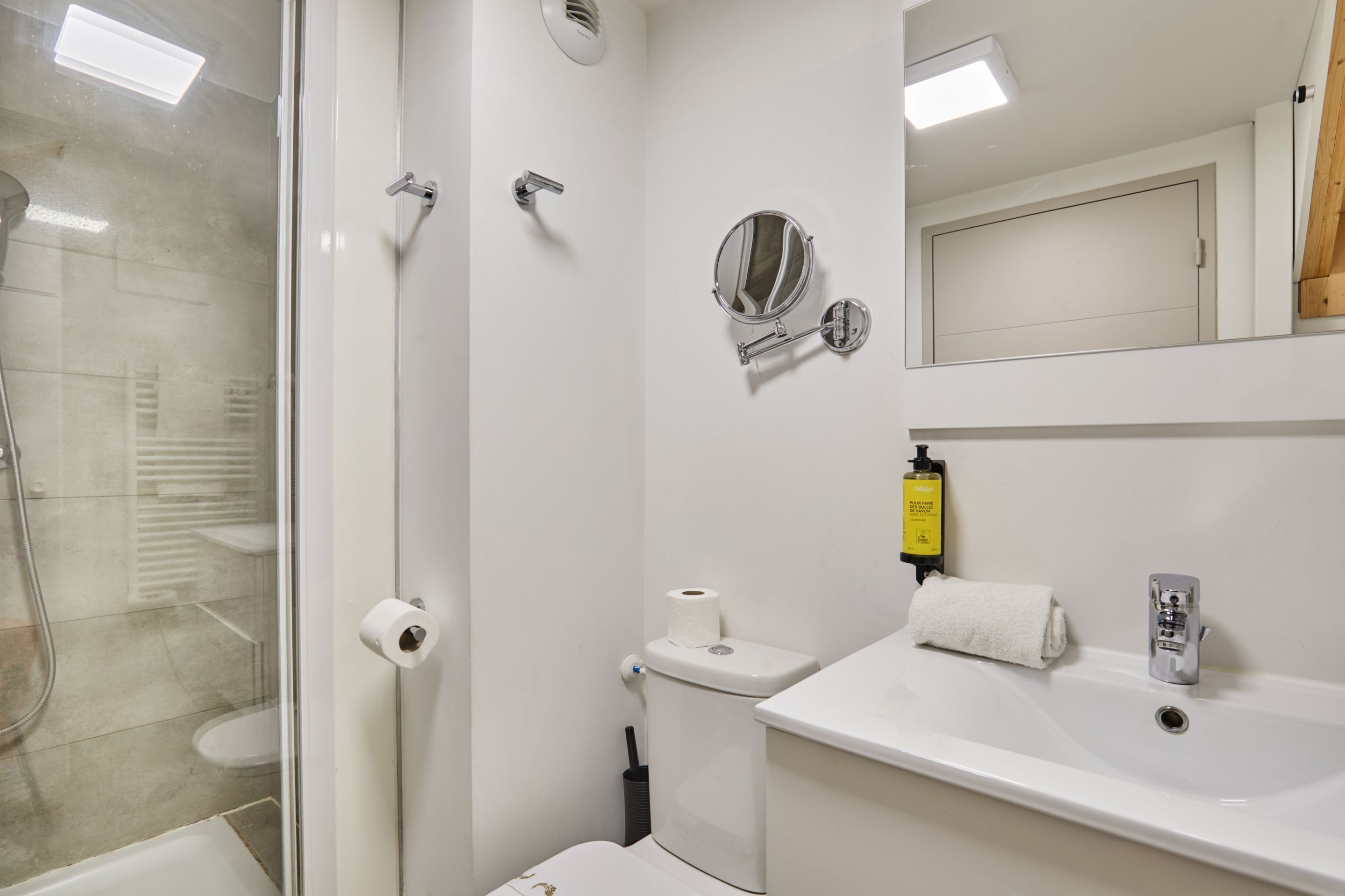 Un baño con cabina de ducha de vidrio, inodoro, lavamanos con espejo y un perchero para toallas.