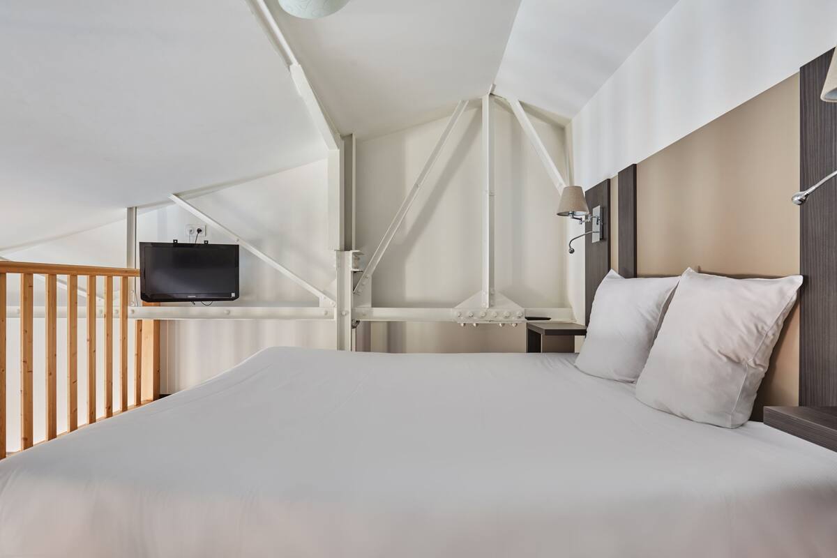Ein modernes Hotelzimmer mit einem großen Bett, einem an einer weißen Wand montierten Fernseher und einem Geländer aus Holzlatten.
