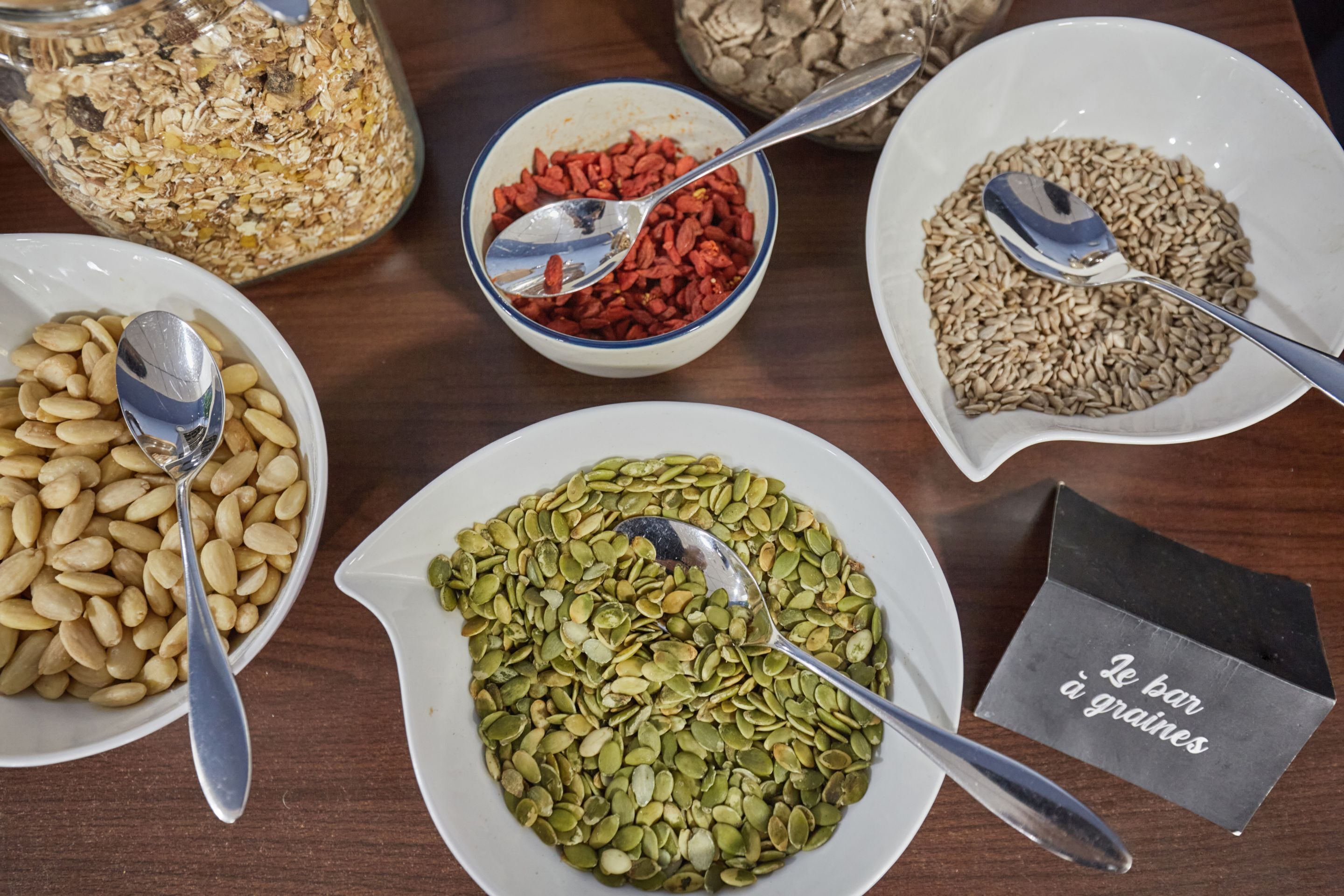 A table with bowls of various grains and seeds, each with a spoon.
