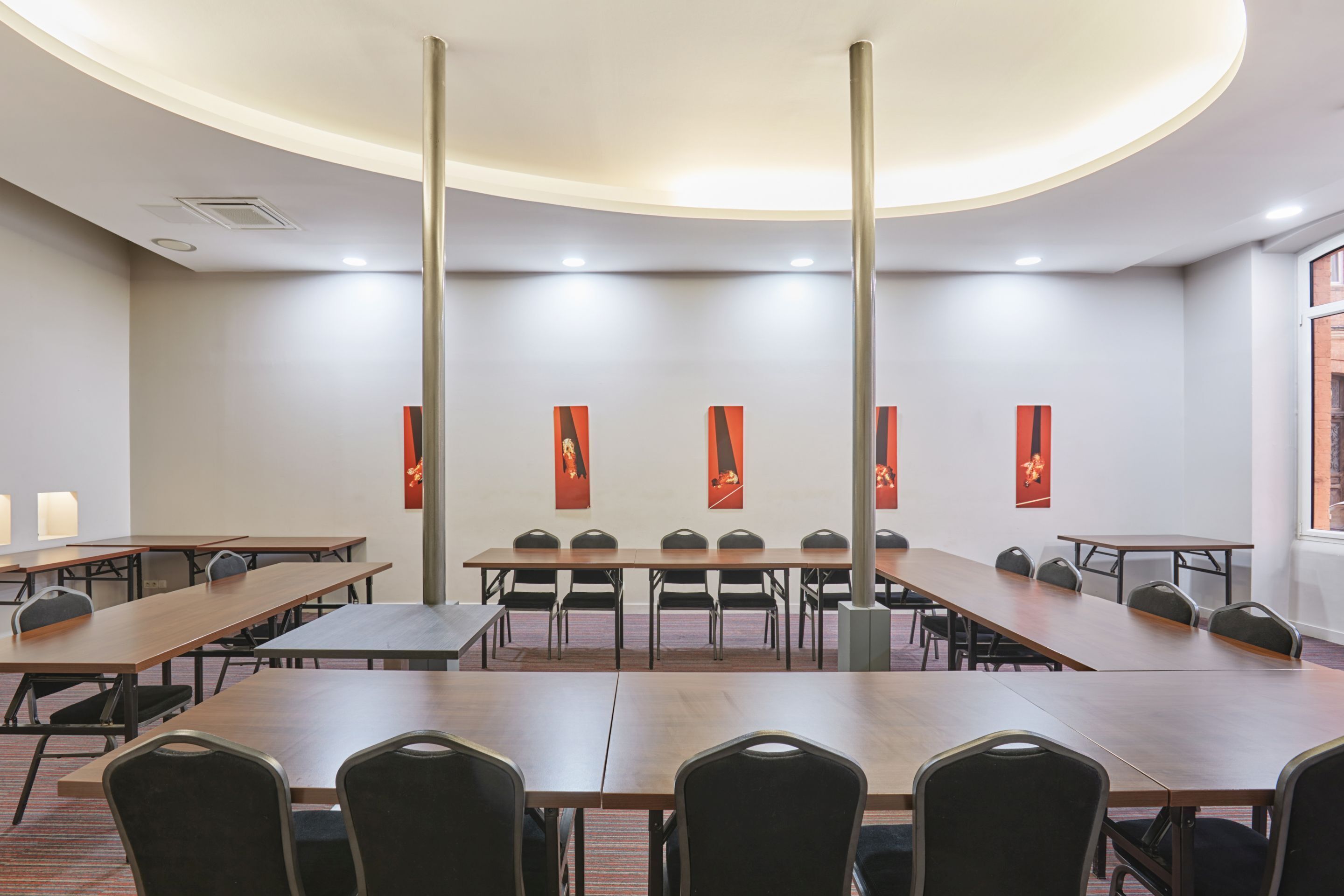 A conference room with long tables and chairs, a curved ceiling, and red banners on the walls.