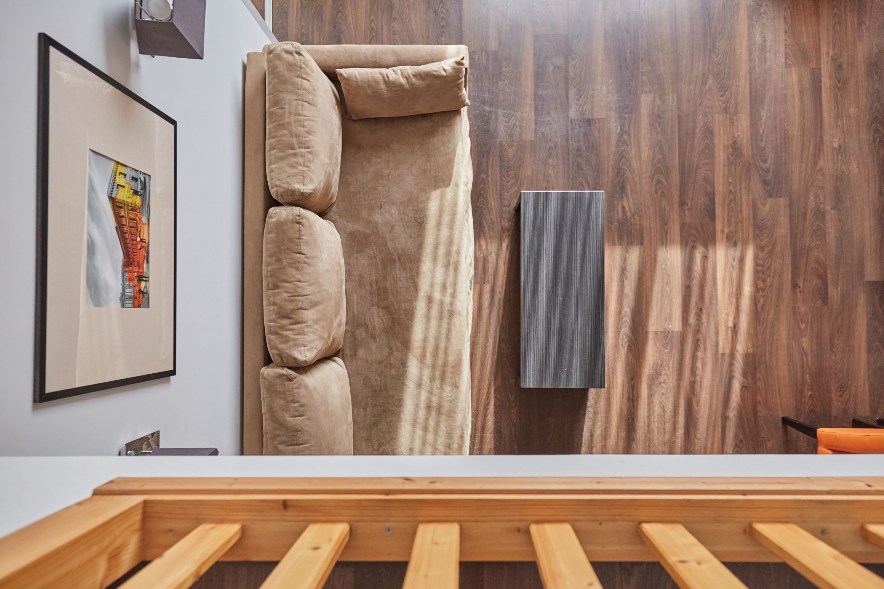 Une pièce avec un cadre de lit en bois, un canapé beige, un panneau mural en bois et un tableau encadré.