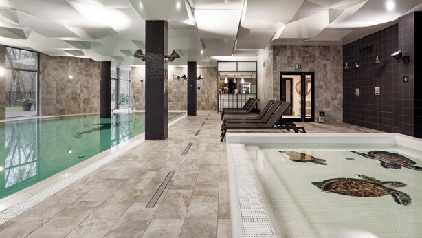 A modern indoor swimming pool with a clear view of the pool area, a separate hot tub with turtle designs, and a spa area with seating. - Diune Resort (Kolobrzeg)