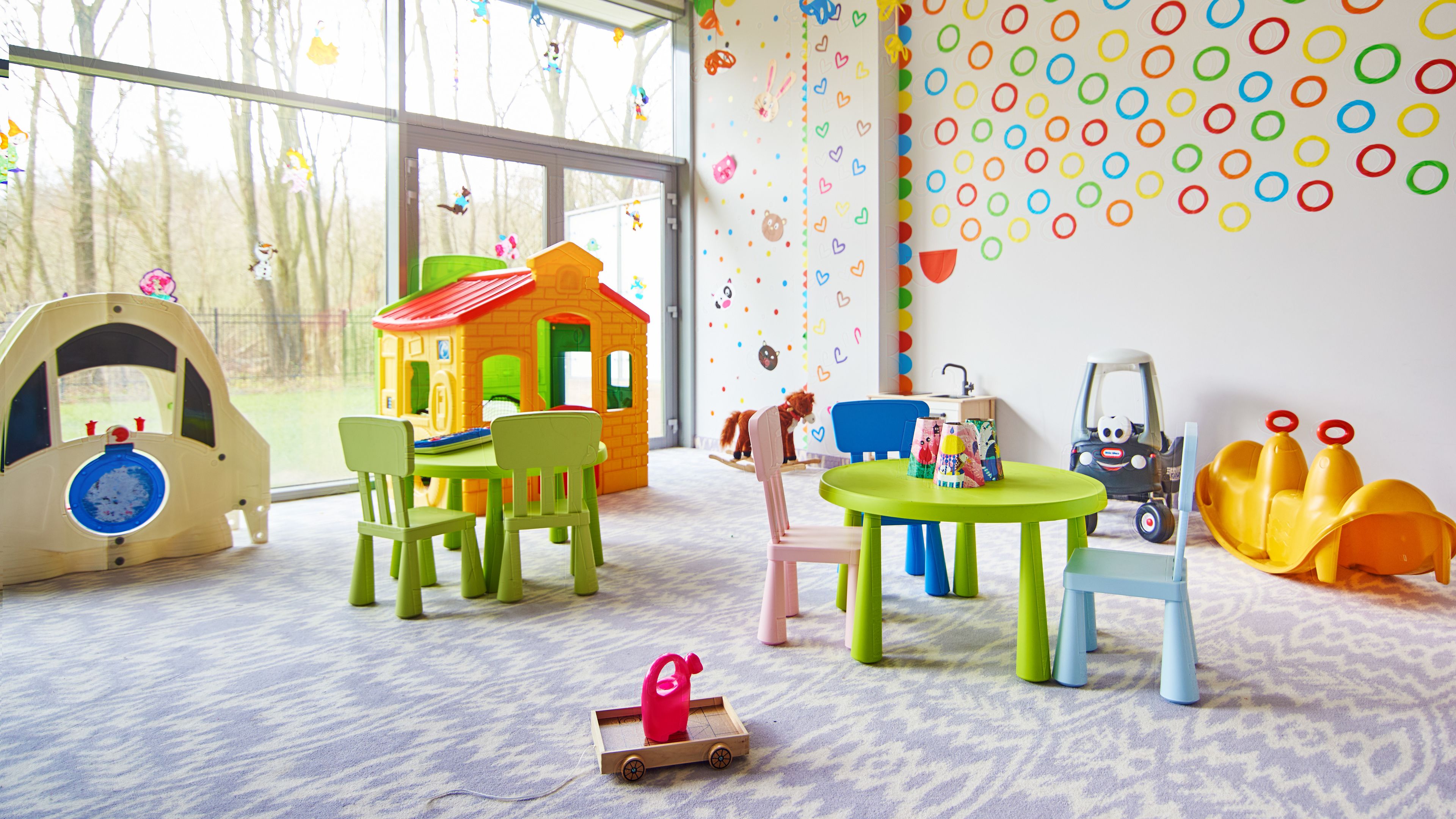 Un cuarto de juegos infantil con una casita de juegos, sillas, una mesa y juguetes.