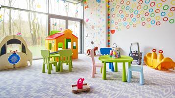 Un cuarto de juegos infantil con una casita de juegos, sillas, una mesa y juguetes.