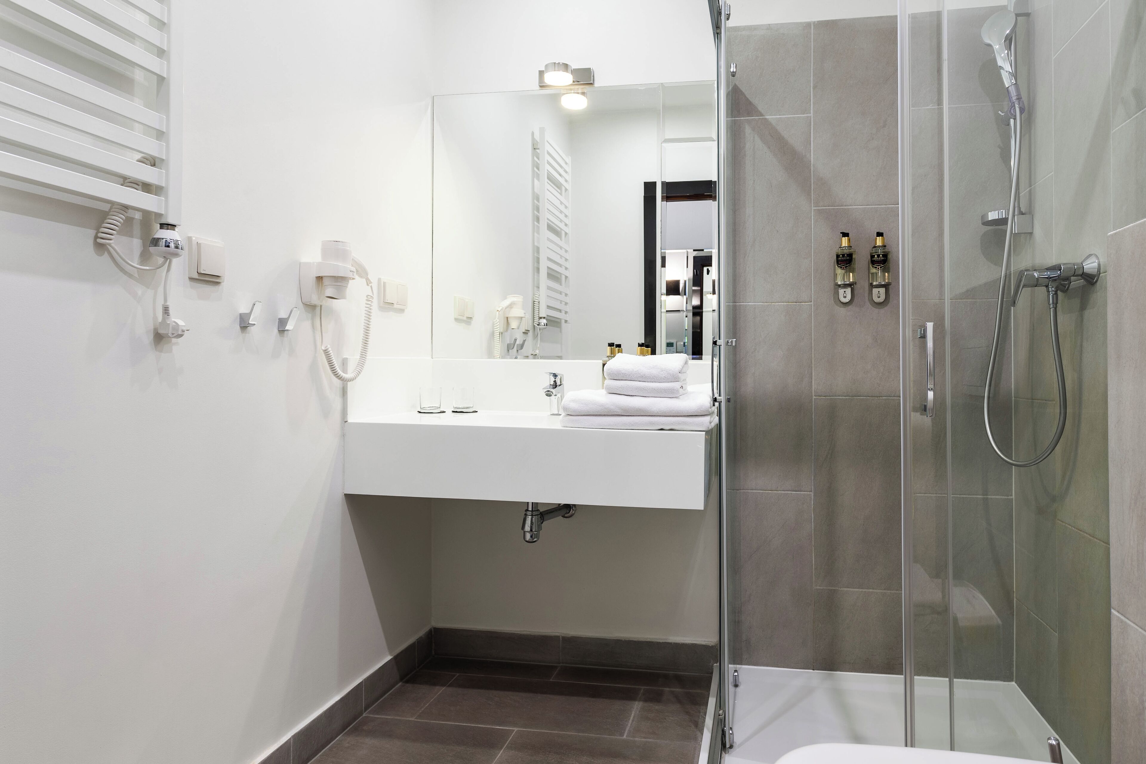 A modern bathroom with a glass-enclosed shower, a white sink with a mirror, and a towel rack.