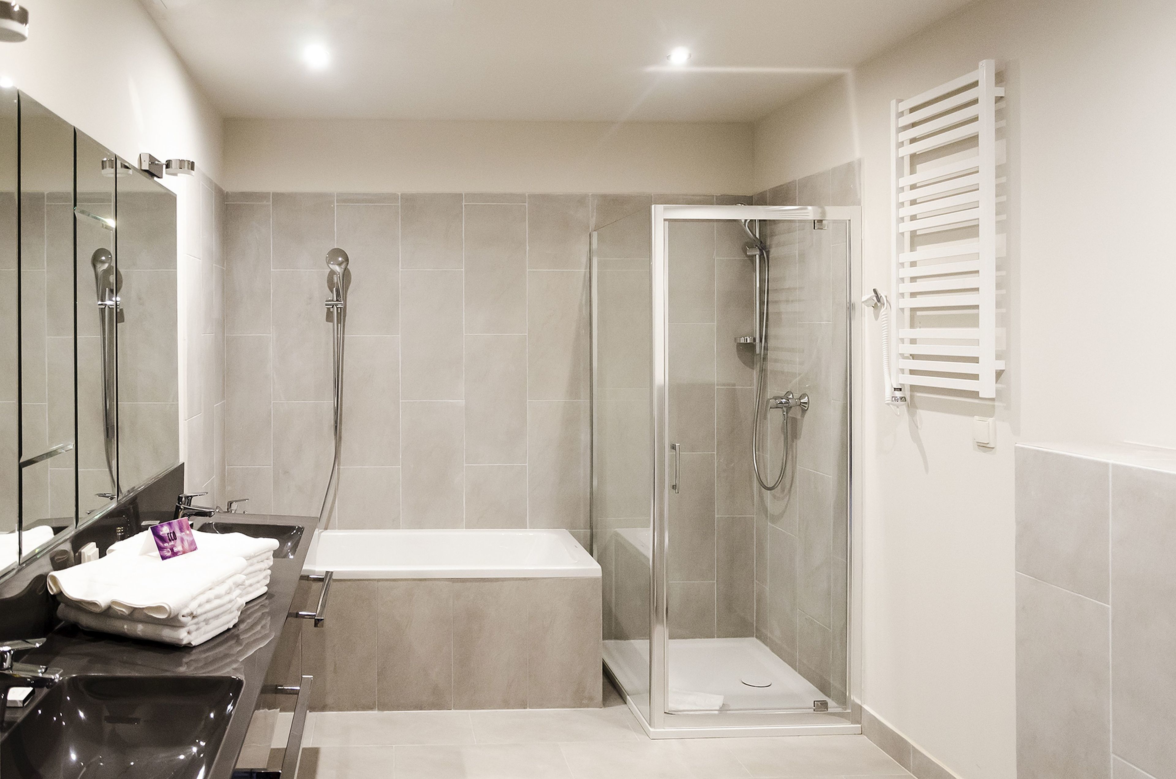 Une salle de bain moderne dotée d’une douche à parois de verre, d’une baignoire et d’un meuble-lavabo avec un miroir et une pile d’essuie-bains.
