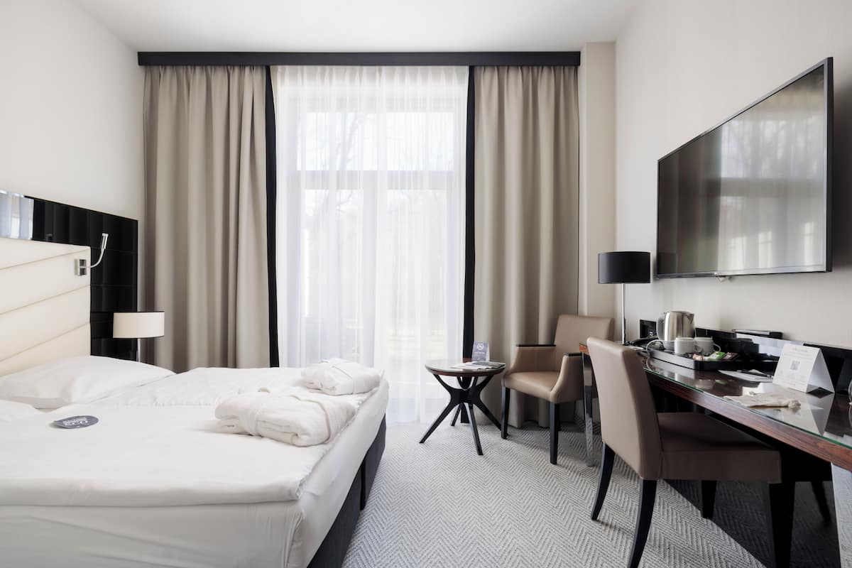 Une chambre d’hôtel équipée d’un lit, d’un bureau, d’une chaise, d’une télévision et d’une fenêtre avec des rideaux.