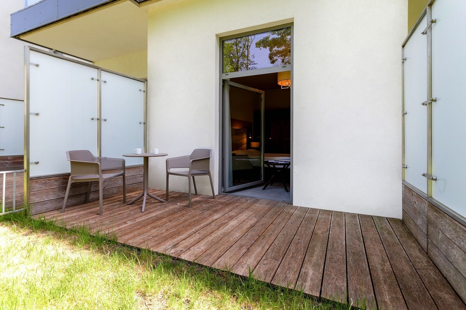 Een modern terras buiten met een houten terras, twee stoelen en een kleine tafel.