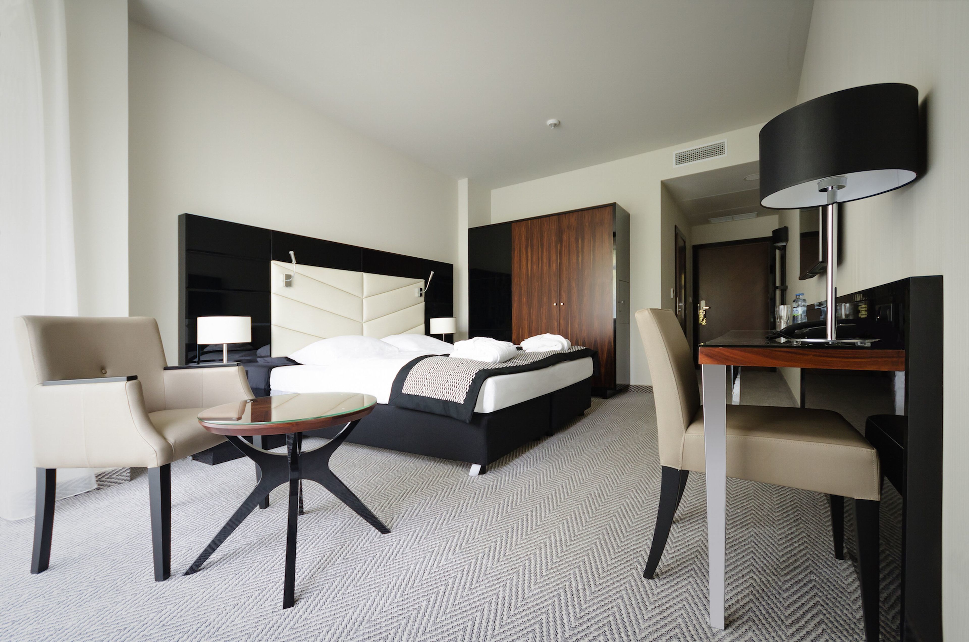 Una habitación de hotel moderna con una cama, dos sillas, una mesita, un escritorio y una lámpara.