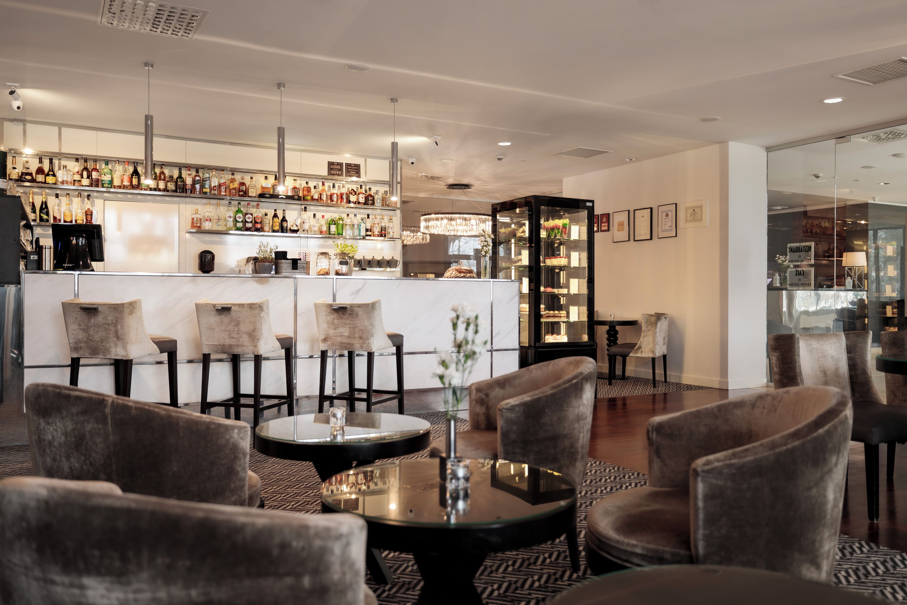 A bar area with a variety of liquor bottles, a counter, and seating with round tables and chairs.