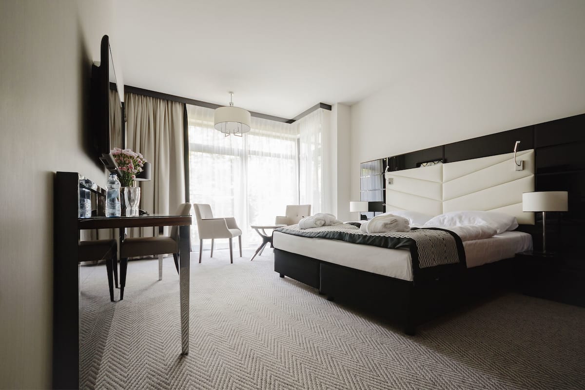 Une chambre d’hôtel avec un lit, un bureau, une chaise, une télévision et une fenêtre avec des rideaux.