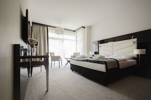 Habitación de hotel con cama, escritorio, silla, televisión y ventana con cortinas.