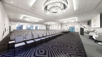 Ein Konferenzraum mit Reihen von Stühlen, einem gemusterten Teppich, Kronleuchtern und einem Schild für DIUNE HOTEL & RESORT.