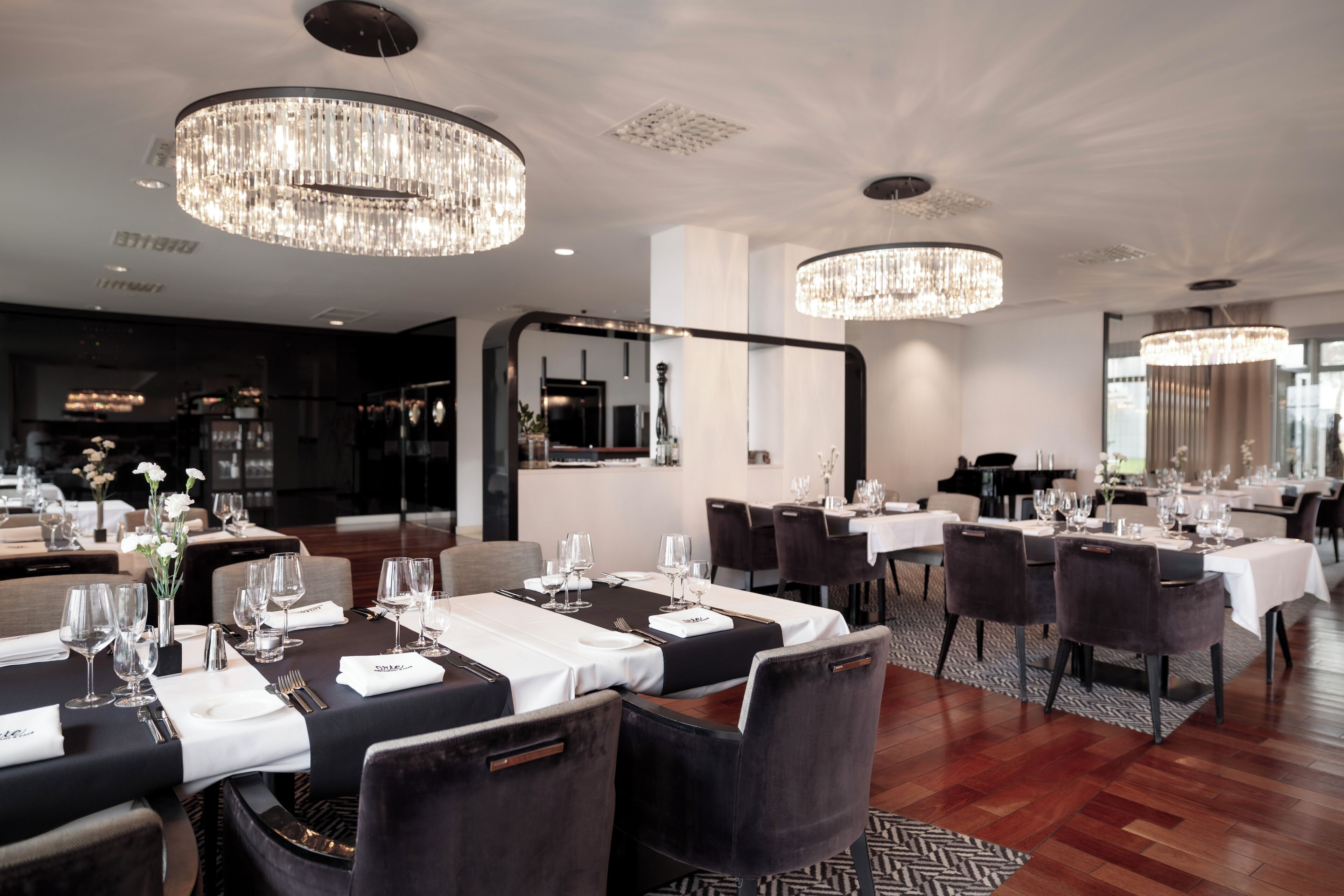 Un comedor moderno con mesas redondas, sillas oscuras y candelabros de cristal.