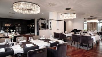 Un comedor moderno con mesas redondas, sillas oscuras y candelabros de cristal.