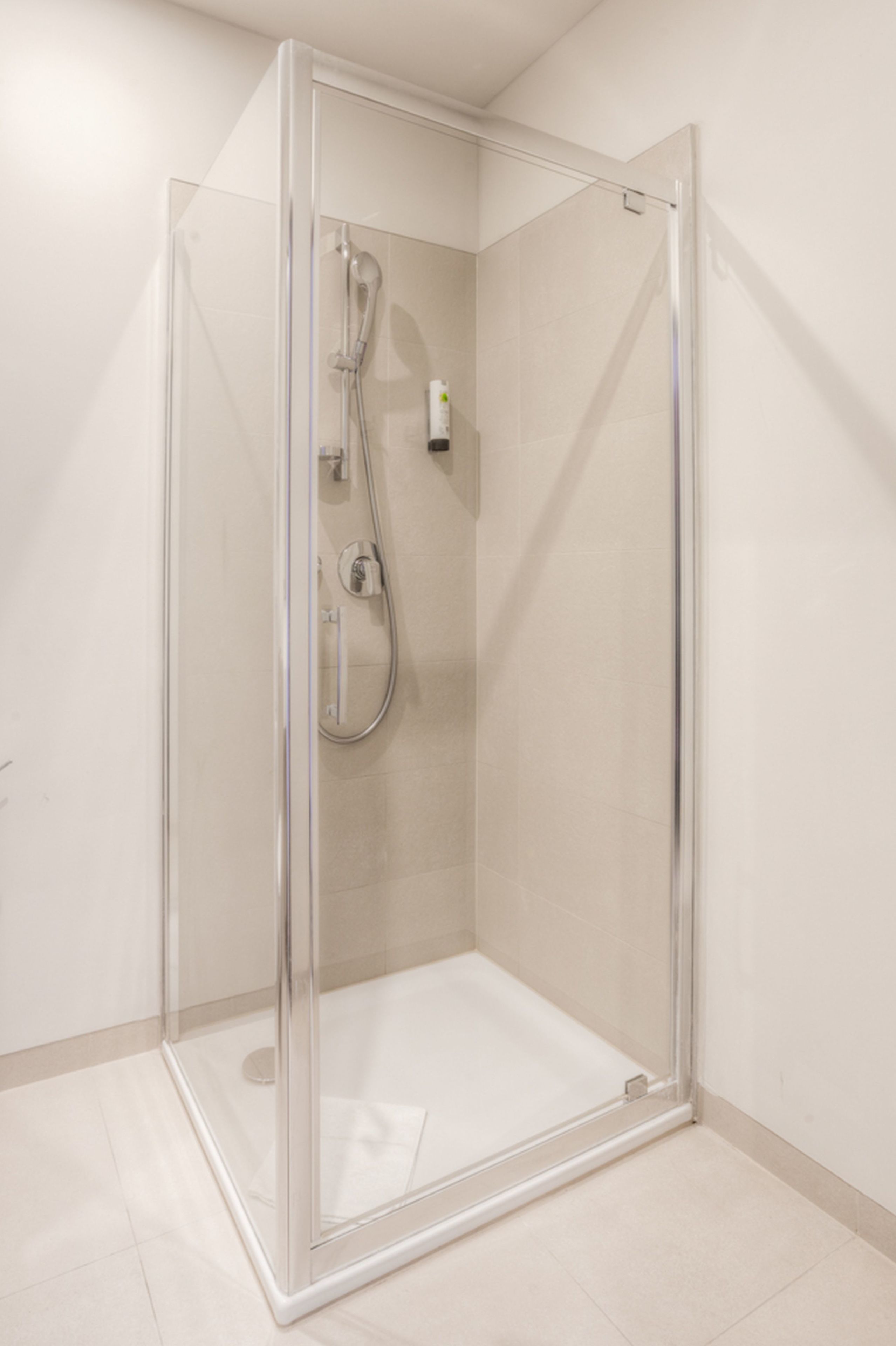 A clear glass shower enclosure with a handheld showerhead and a wall-mounted control panel.