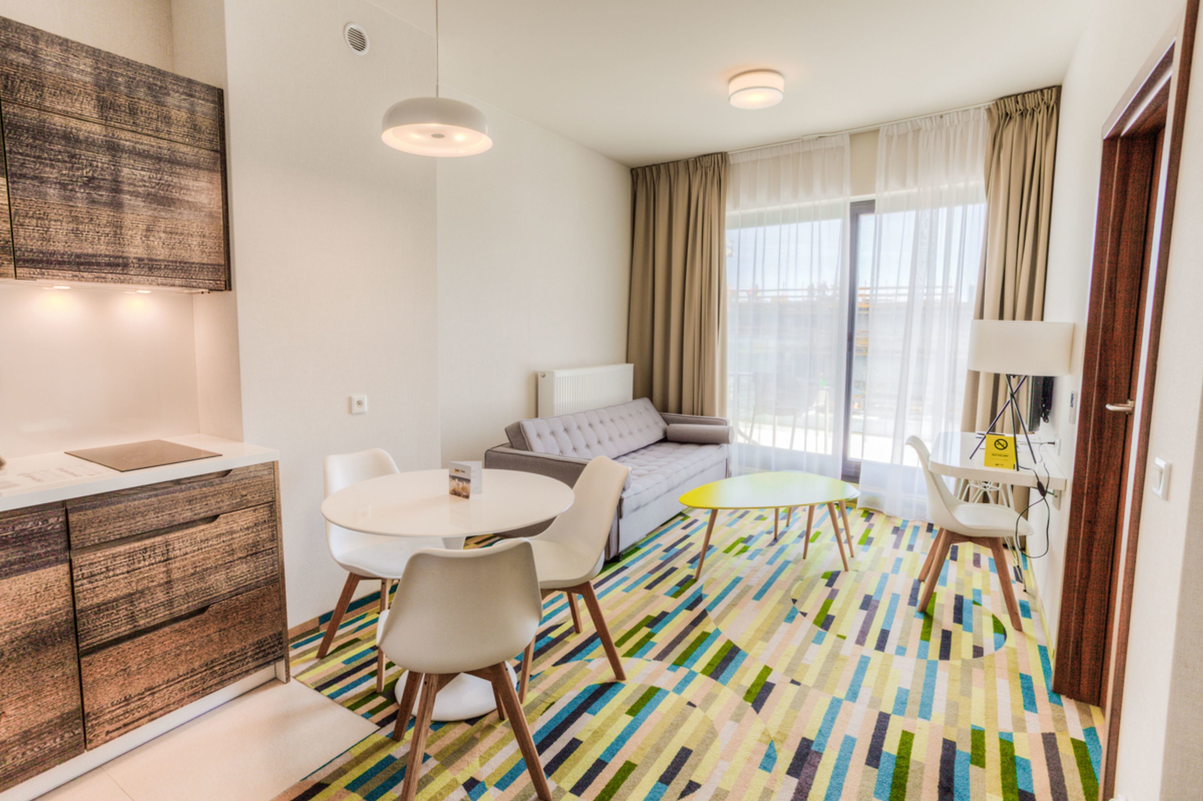Una habitación de hotel moderna con sofá, una mesa de comedor y una pequeña cocina.