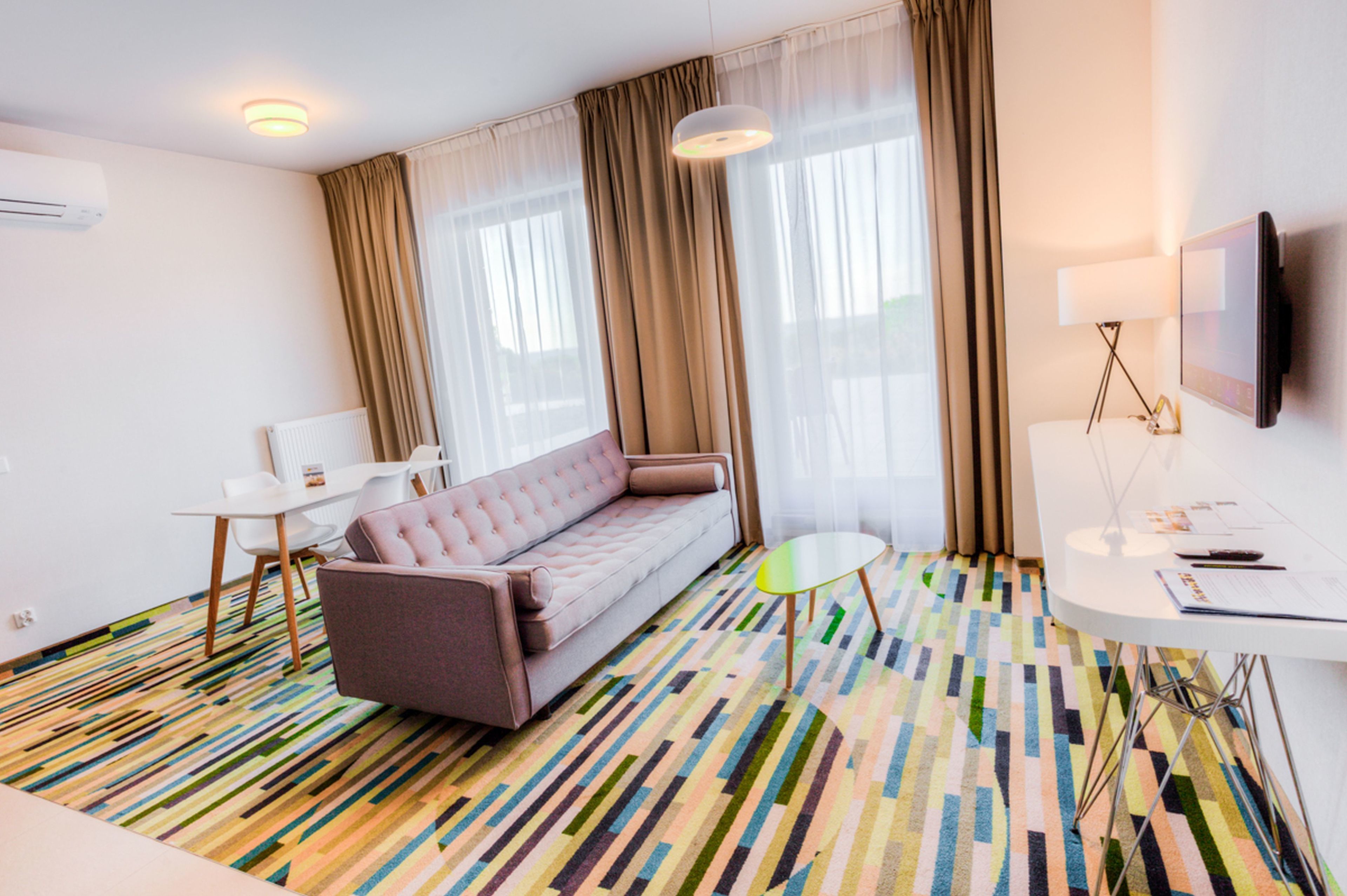 Et moderne hotelværelse med en sofa, et lille bord, et fjernsyn og et mønstret tæppe.