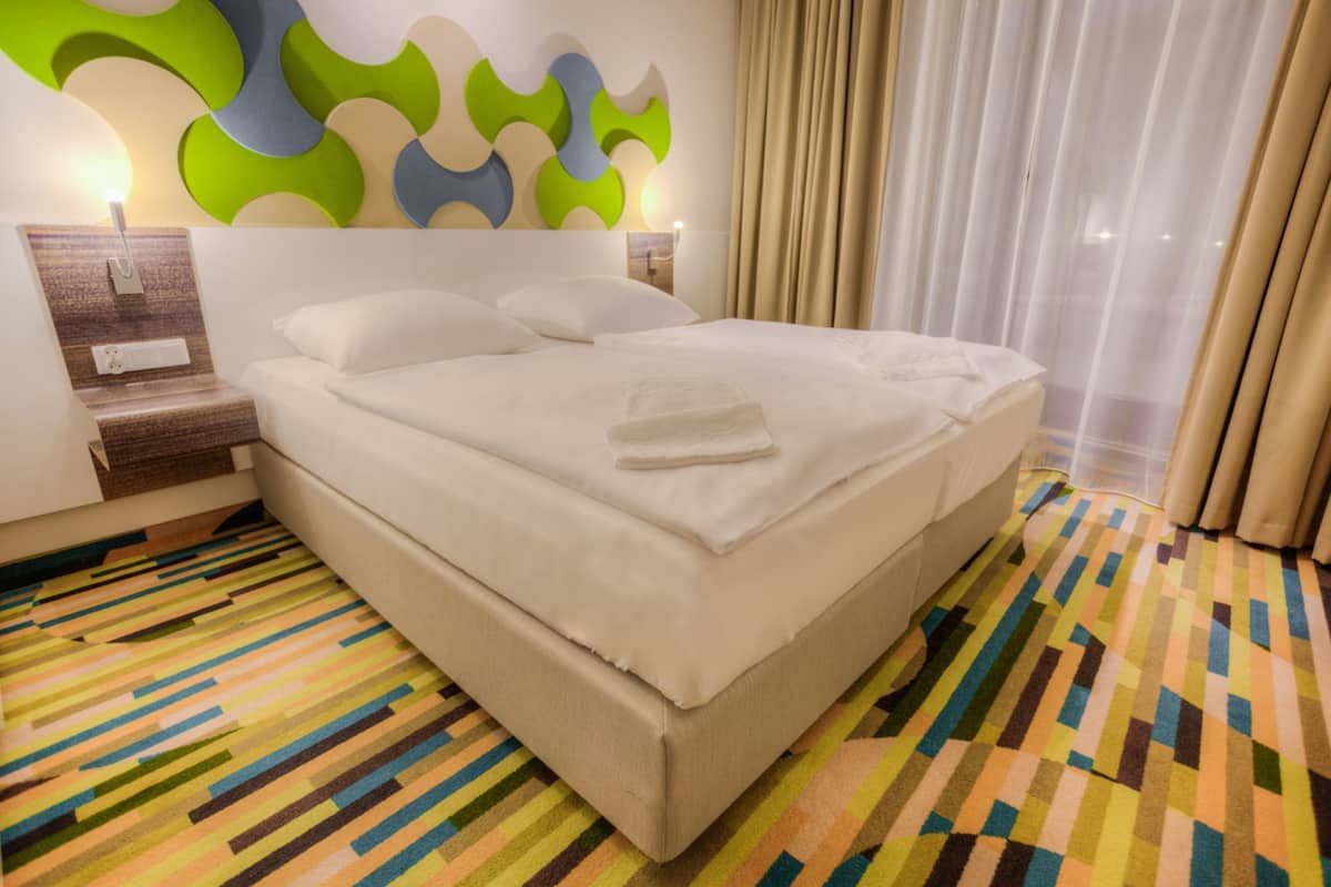 Ein Hotelzimmer mit einem großen Bett, einer Wandlampe, einem Nachttisch und einem gemusterten Teppich.
