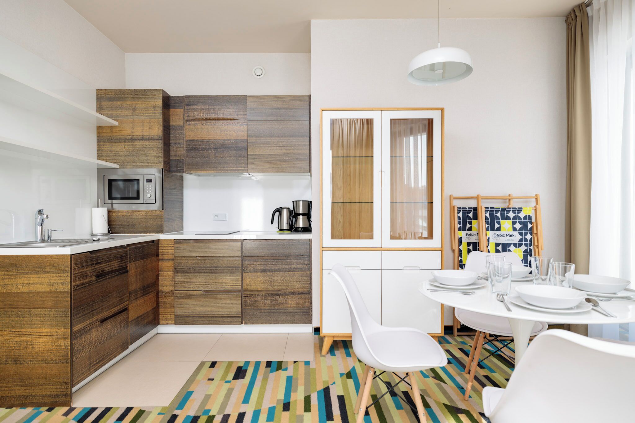 Een moderne keuken met houten kastjes, een magnetron en een eethoek met een ronde tafel en stoelen.