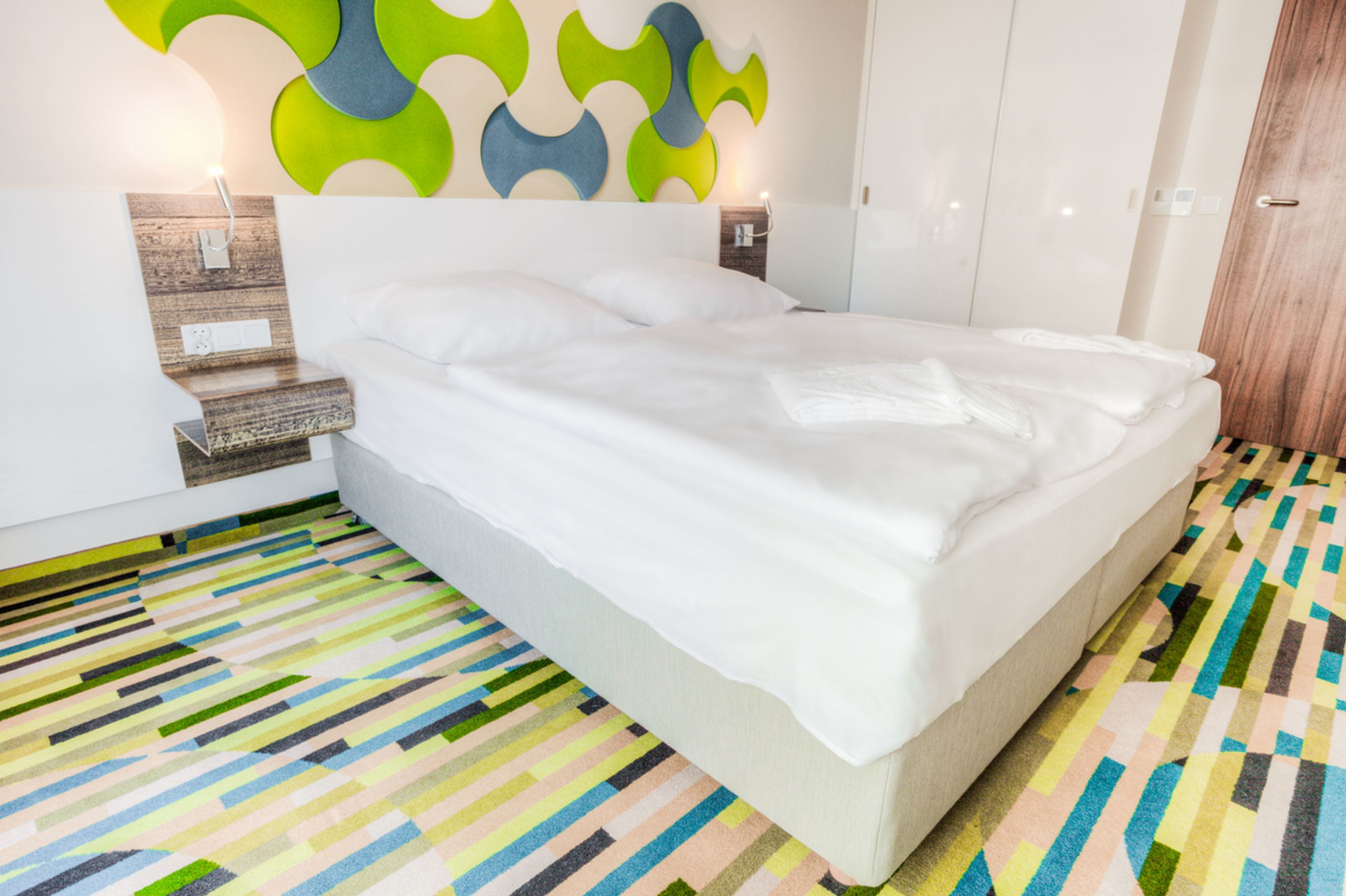 Una habitación de hotel moderna con una cama grande, una alfombra colorida a rayas y un diseño de pared original.