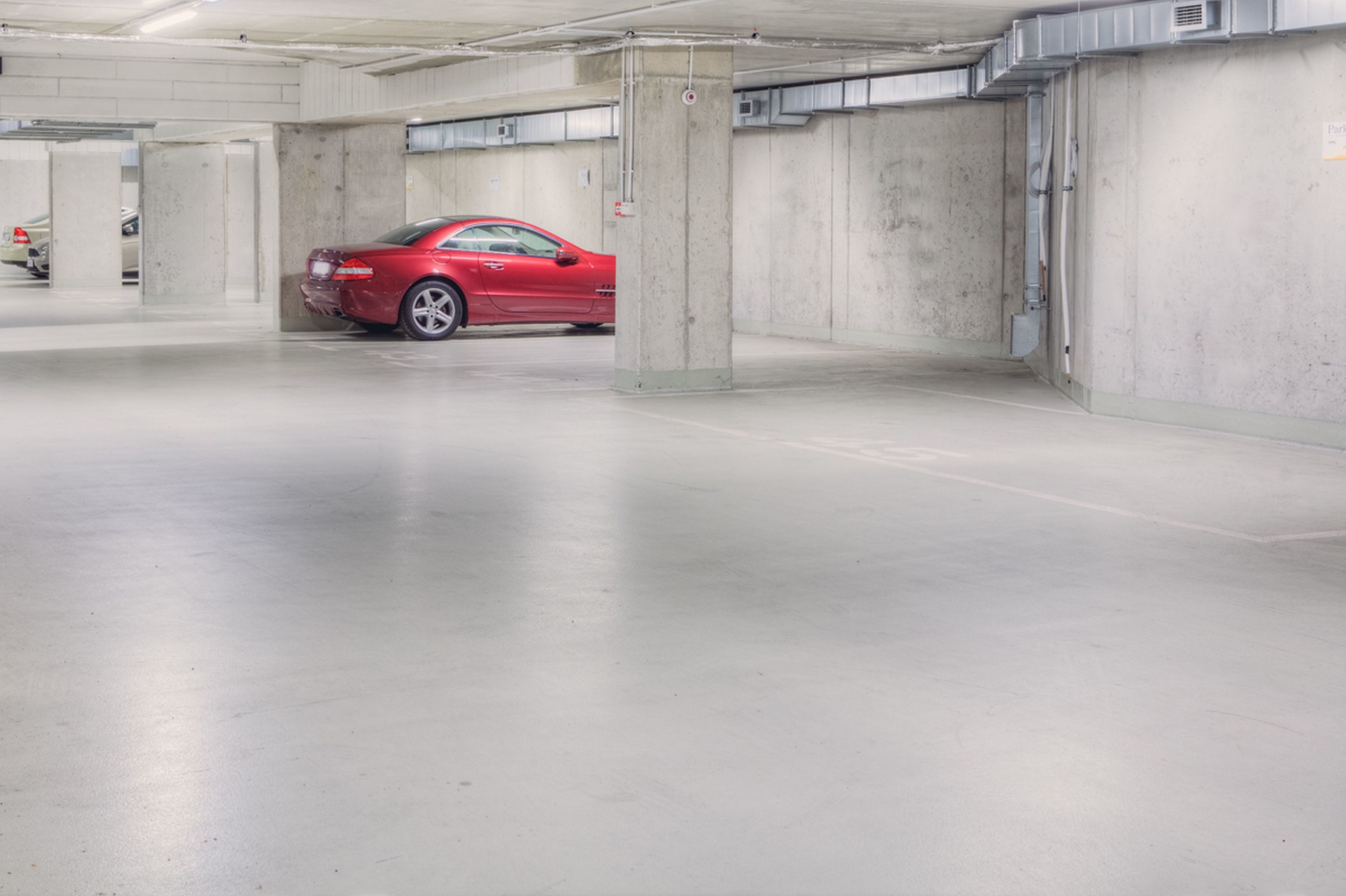 Eine Parkgarage mit Betonpfeilern und einem roten Auto in einem Stellplatz.