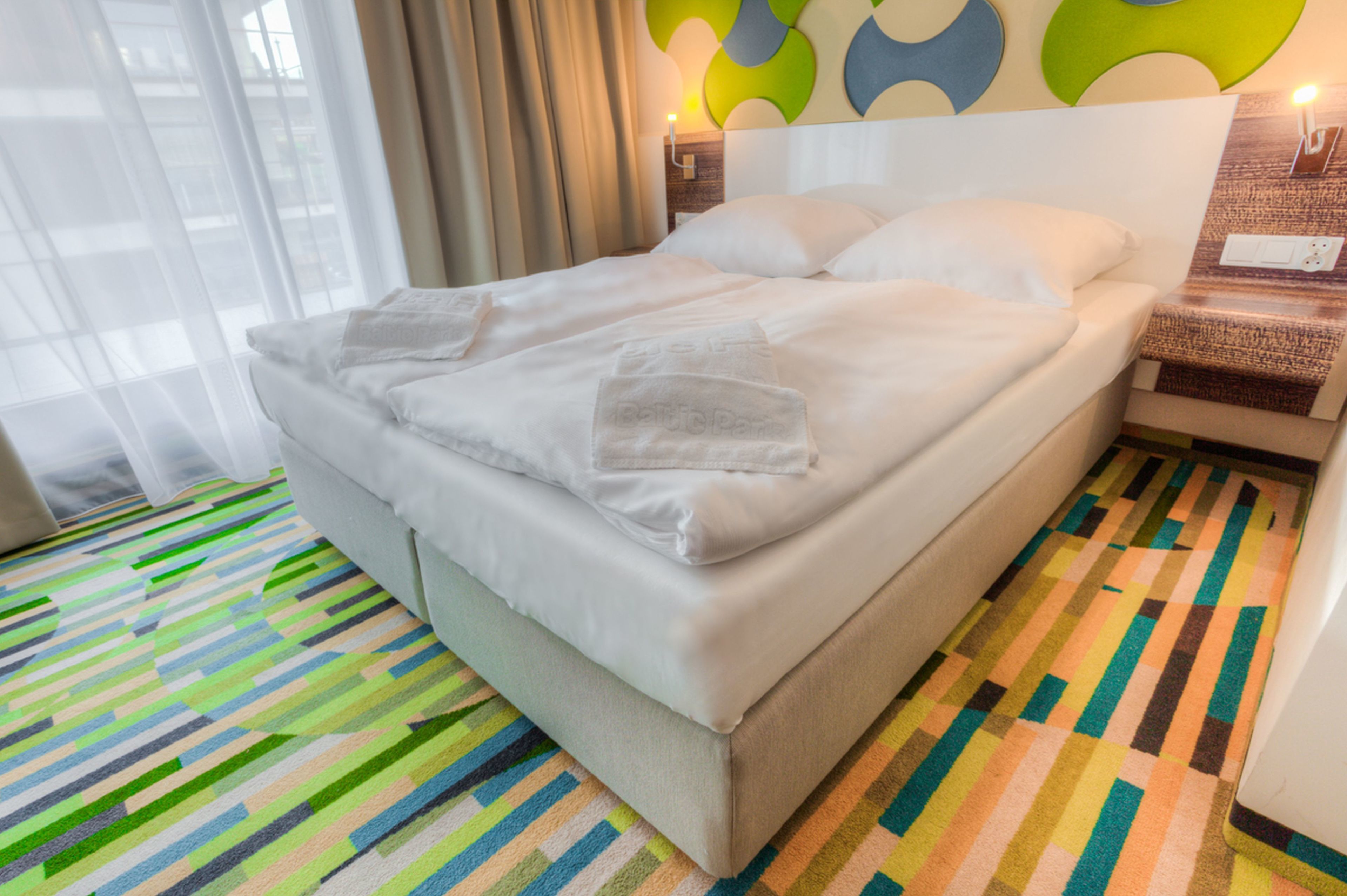 Ein ordentlich bezogenes Bett mit weißen Leinen und Handtüchern, ein farbenfroher Streifen Teppich und ein modernes Wanddesign.