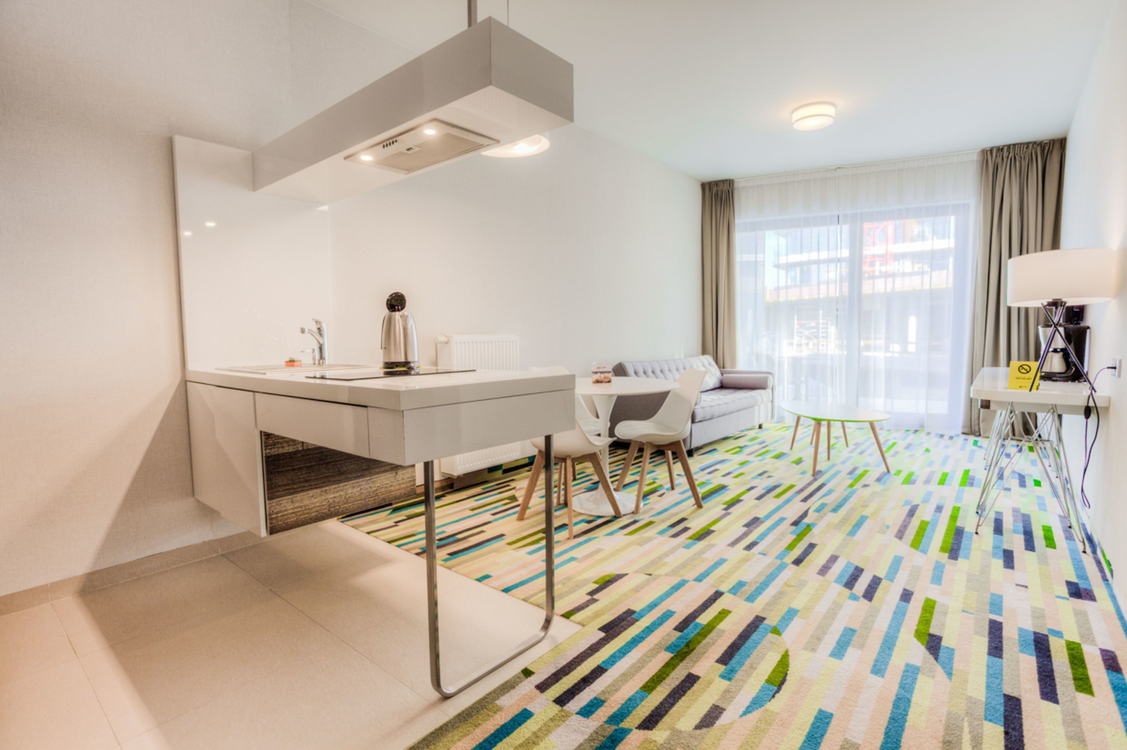 Una camera d'hotel moderna con una scrivania bianca, una sedia, un tavolino e un divano.