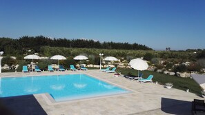 A pool area with lounge chairs and umbrellas, surrounded by greenery and a clear sky. - Agriturismo Li Damiani (Otranto)