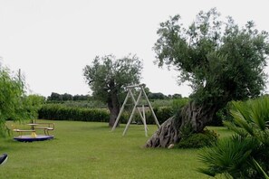 Eine grüne Außengelände mit Schaukel, Bank und einem großen Baum.