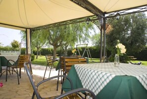 An outdoor patio area with tables and chairs, covered by a canopy, and surrounded by greenery. - Agriturismo Li Damiani (Otranto)