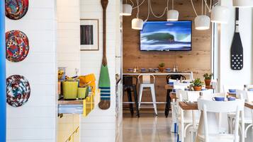 Ein Restaurant mit einer Holzwand, einem Fernseher, der eine Welle zeigt, und weißen Stühlen mit blauen Akzenten.