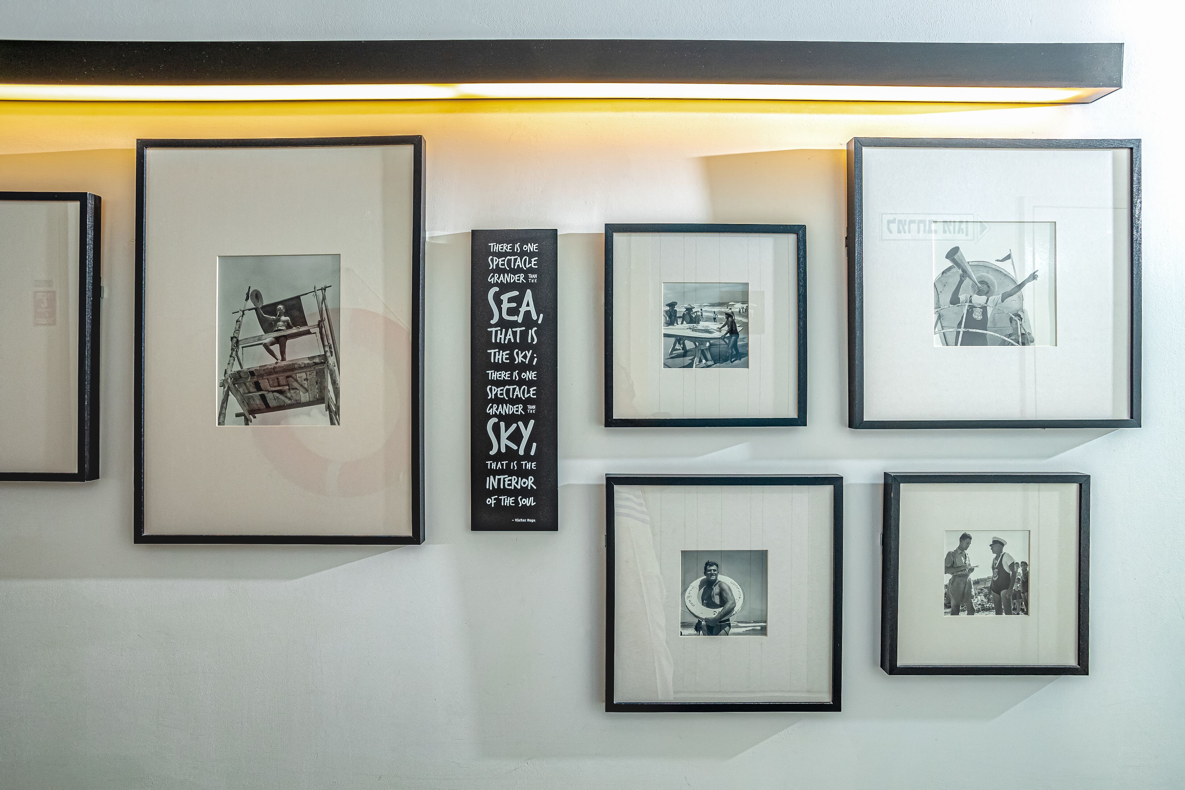 A wall with framed photographs and a quote about the sea and sky.