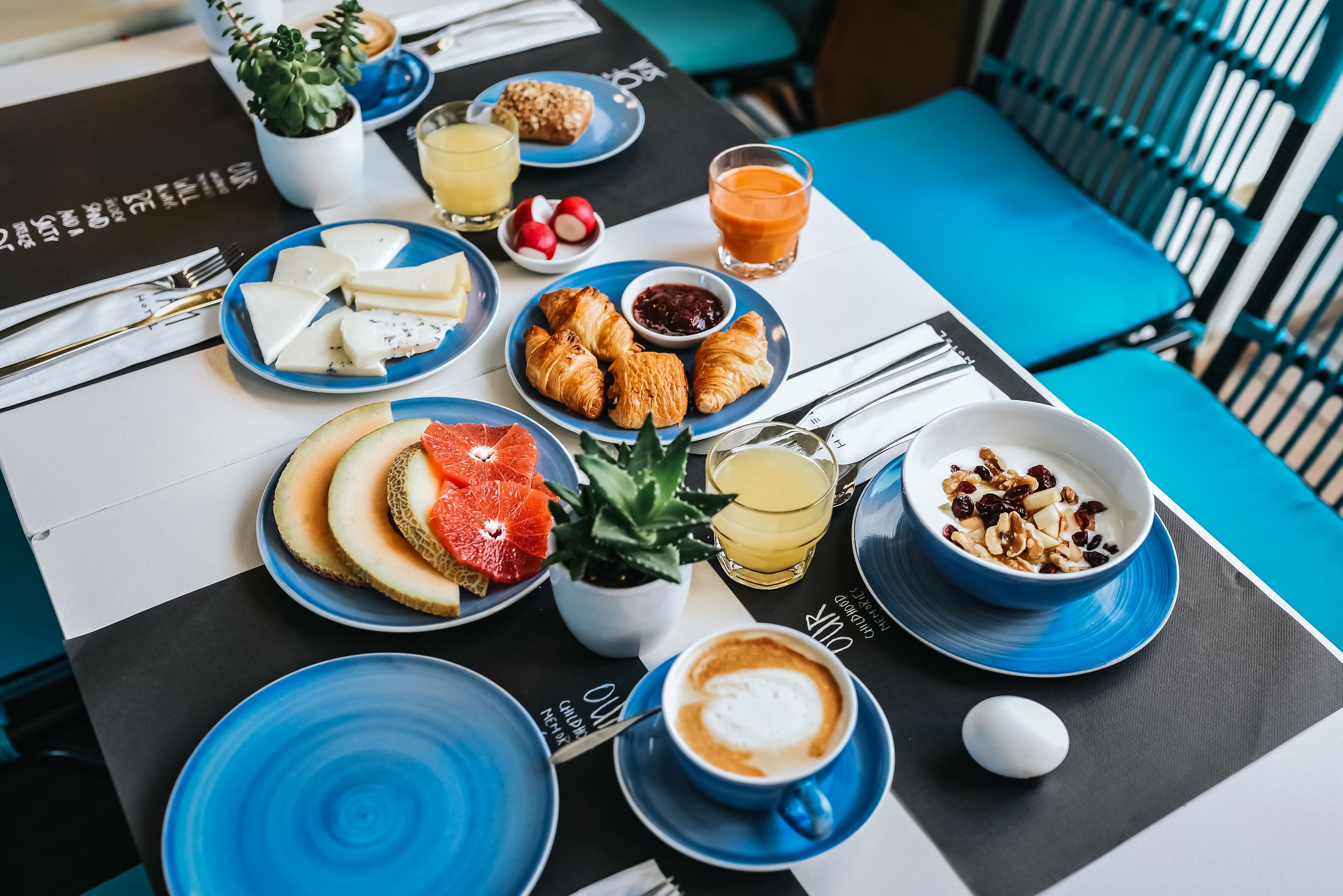 A breakfast table with plates of cheese, croissants, fruit, and coffee.