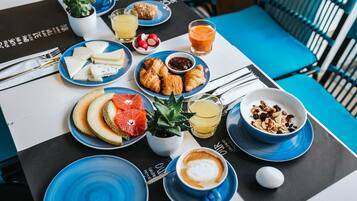 A breakfast table with plates of cheese, croissants, fruit, and coffee.