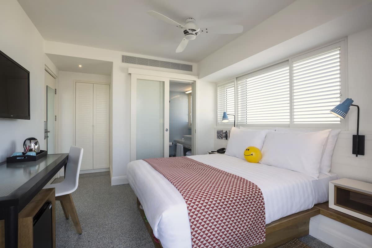 Un dormitorio con cama, escritorio, silla, ventilador de techo y ventana con persianas.