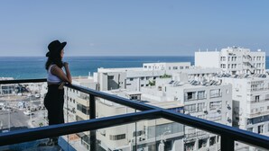 Una persona de pie en un balcón con vistas a un paisaje urbano, edificios y el mar.
