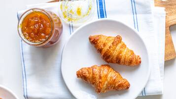 Two croissants on a white plate with a jar of jam and a small bowl of cream.