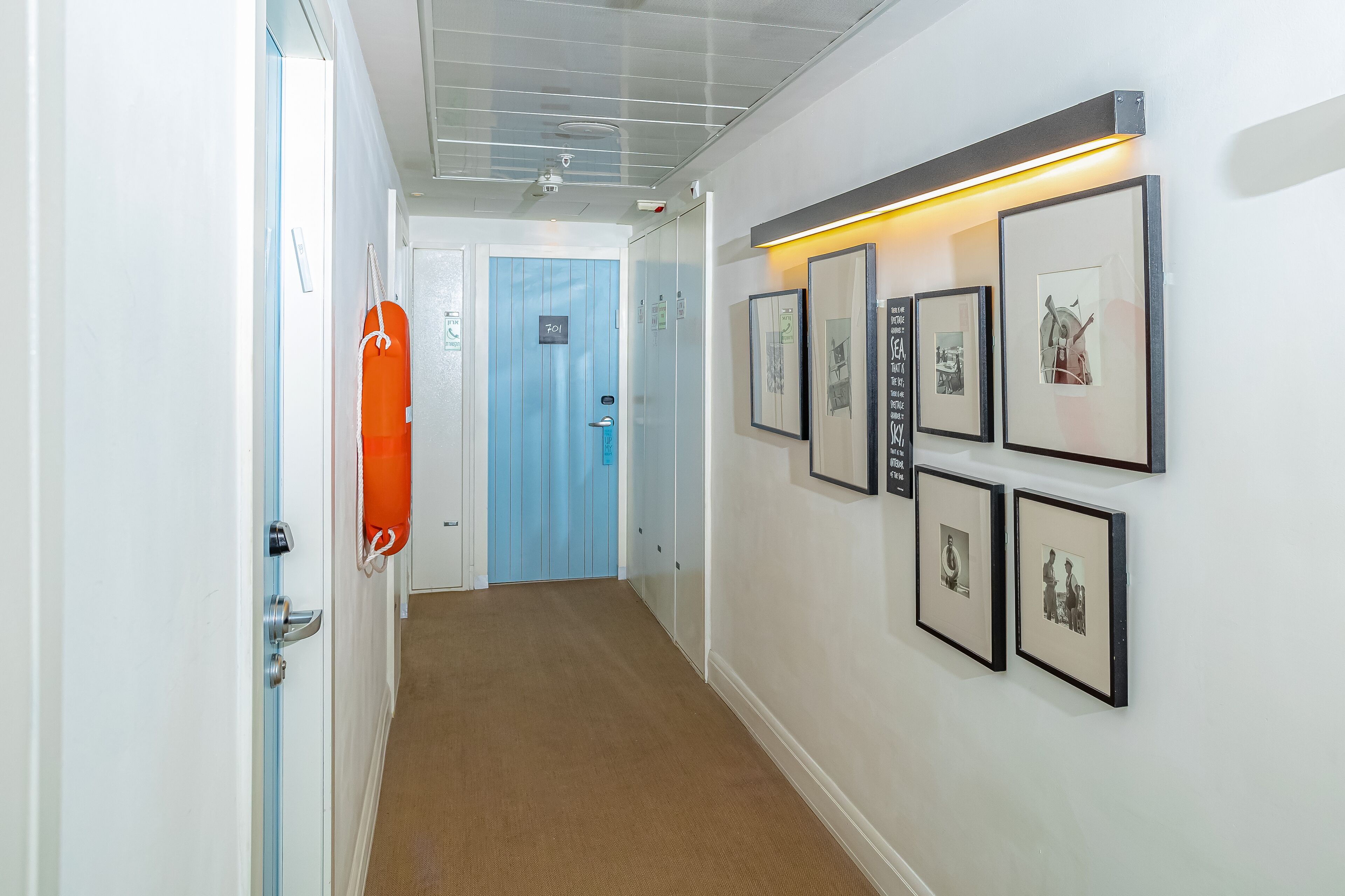 Um corredor com porta azul, quadros nas paredes e um colete salva-vidas laranja pendurado na porta.