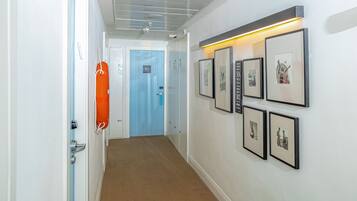 Um corredor com porta azul, quadros nas paredes e um colete salva-vidas laranja pendurado na porta.