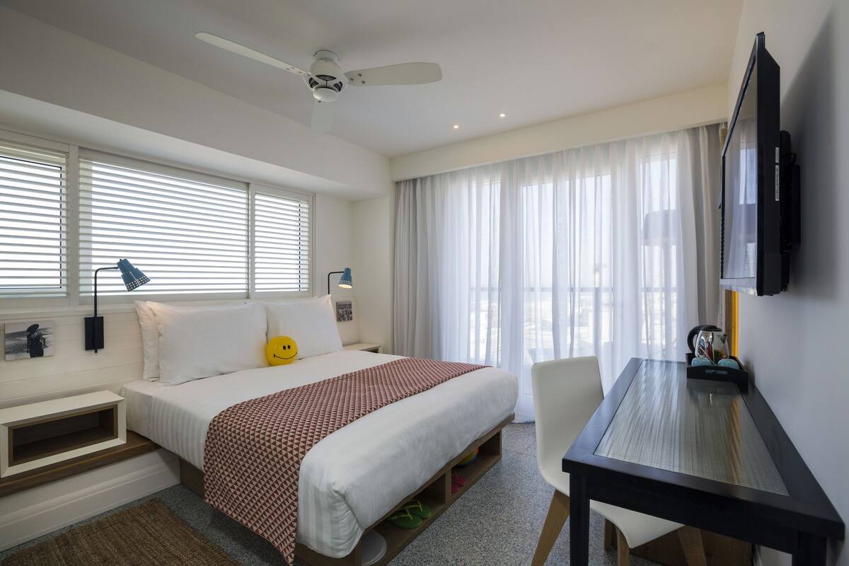 Una habitación de hotel con una cama, un escritorio, un televisor y un ventilador de techo.