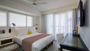 A hotel room with a bed, a desk, a television, and a ceiling fan.