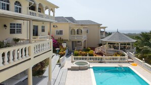 A large, multi-story hotel with a swimming pool, outdoor seating, and a view of the ocean. - The Royal Kensington Villa (Montego Bay)