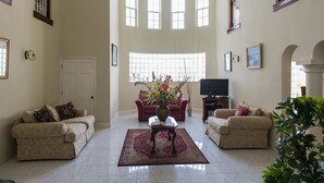 A spacious living room with two sofas, a coffee table, and a large window with multiple panes. - The Royal Kensington Villa (Montego Bay)