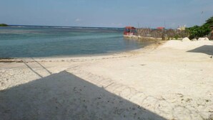 A beach with clear turquoise water, a sandy shore, and a small structure with a red roof in the distance. - The Royal Kensington Villa (Montego Bay)