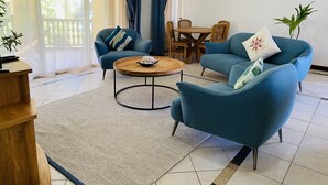 Una sala de estar con sofá, sillón, mesa de centro y una mesa de comedor con sillas.